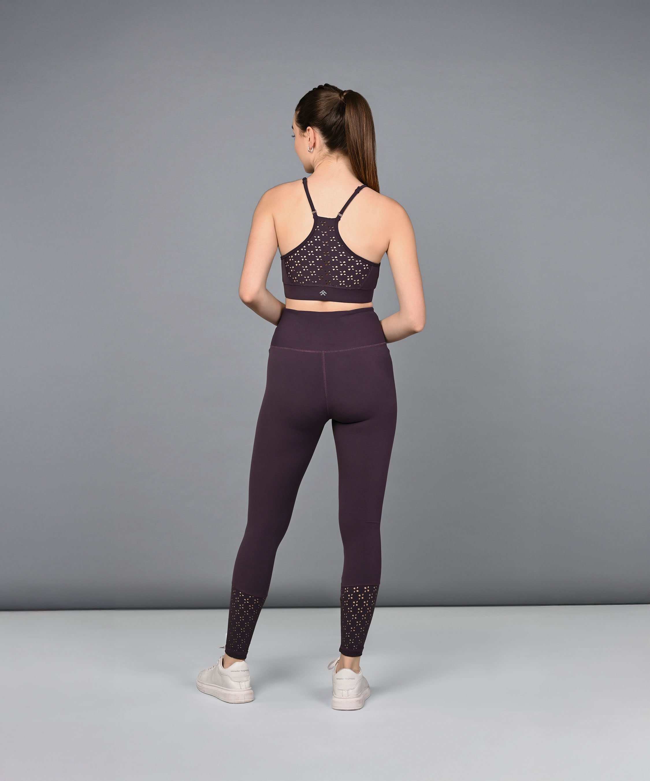 A woman wearing Wine Leggings stands facing away with her hands behind her back, set against a plain gray background.
