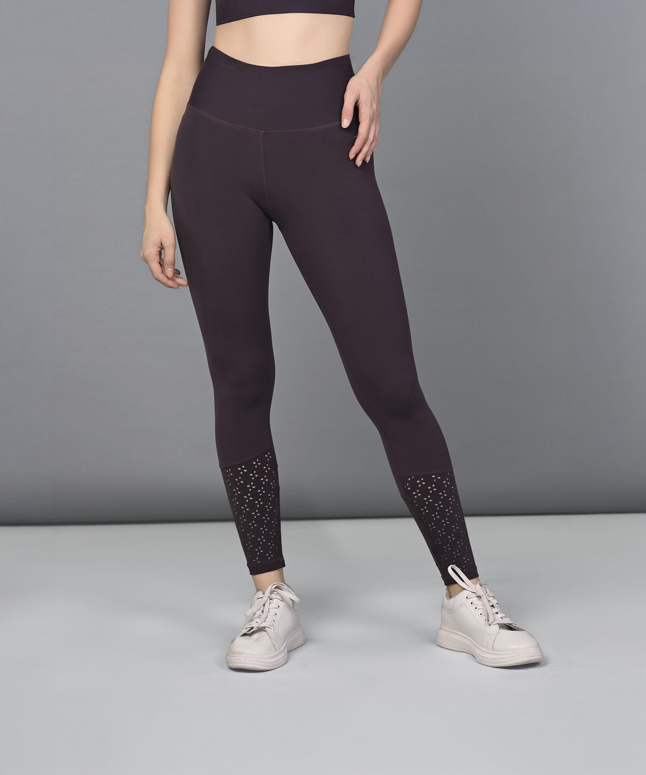 A woman models the Wine Leggings, featuring a dark botanical print and studded ankle details, paired with white sneakers against a gray background.