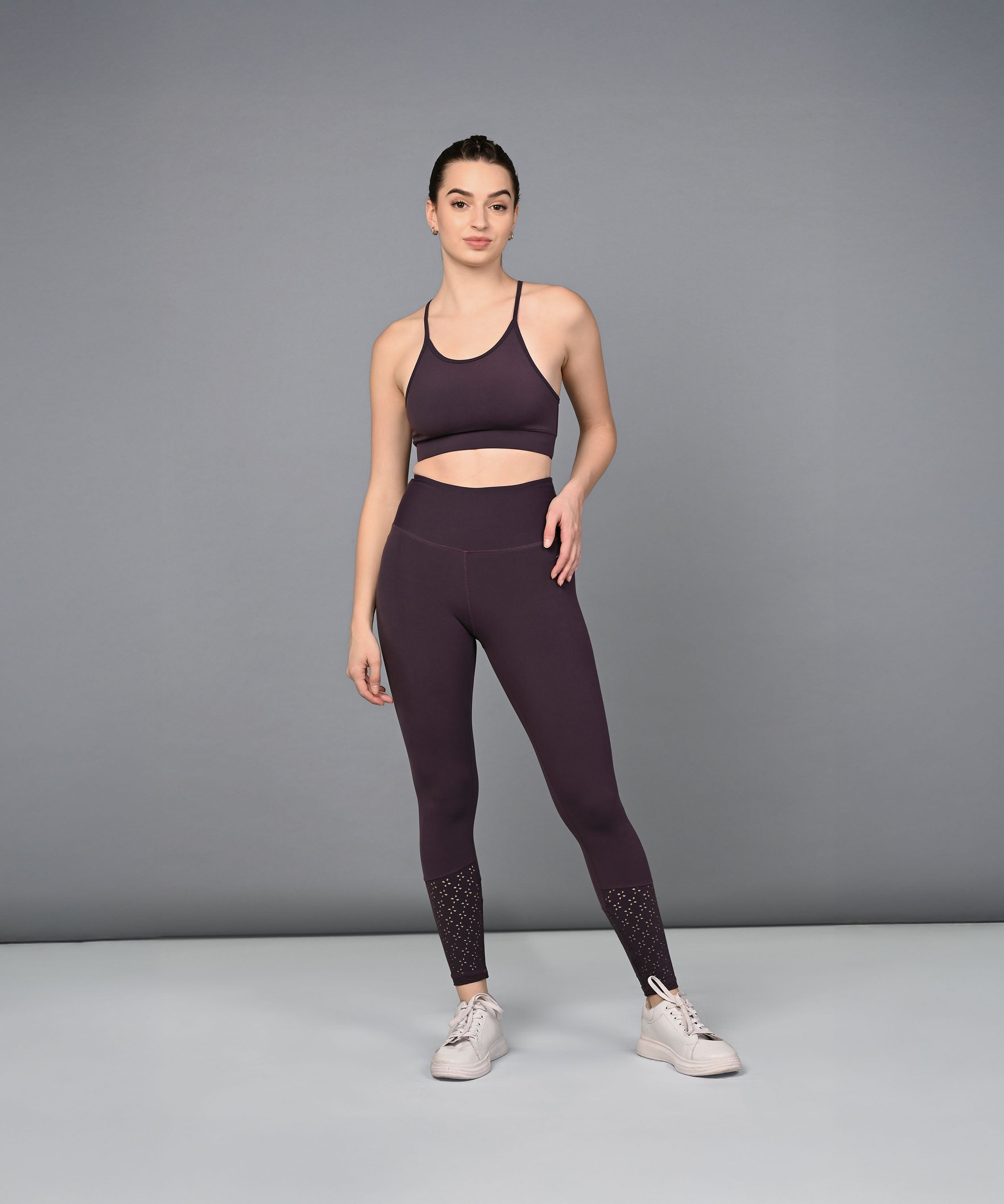 A woman in a dark purple sports bra and Wine Leggings stands against a plain gray background.