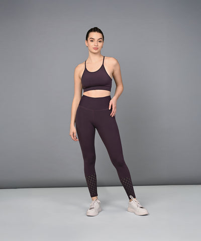 A woman in a dark purple sports bra and Wine Leggings stands against a plain gray background.