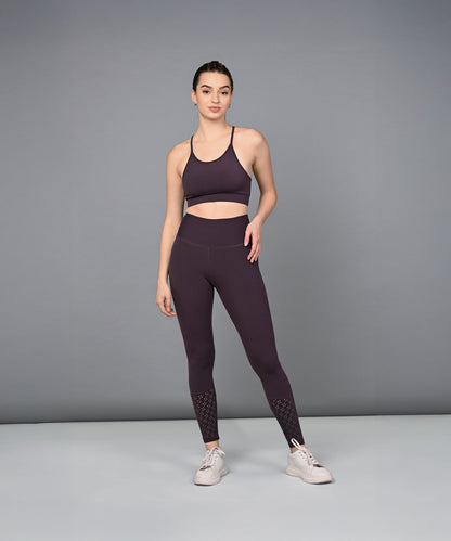 A woman in a dark purple sports bra and Wine Leggings stands against a plain gray background.
