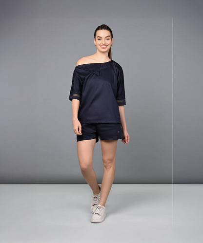 A woman smiles wearing the Off Shoulder Nebula Navy Co-ord set, crafted from 100% cotton, as she poses against a plain gray background.