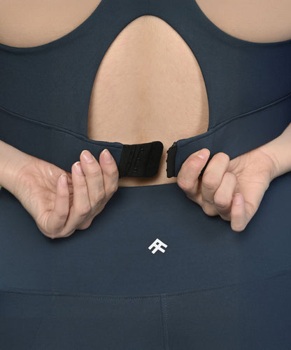 Close-up of hands fastening the back of a teal, moisture-wicking Teal Sports Bra, with a small logo visible on the leggings below.
