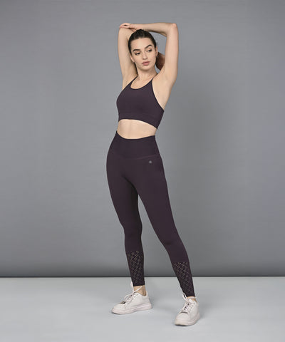 Woman wearing a Wine Netted Top and matching leggings with a honeycomb pattern, striking a pose against a gray background in white sneakers.