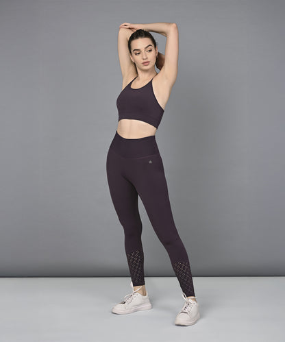 Woman wearing a Wine Netted Top and matching leggings with a honeycomb pattern, striking a pose against a gray background in white sneakers.