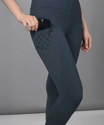 A person pairs a teal netted top with dark leggings featuring a laser-cut floral design and a convenient phone side pocket.