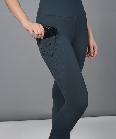 A person wears Teal Leggings with a high-rise waistband, placing a phone into the convenient side pocket.