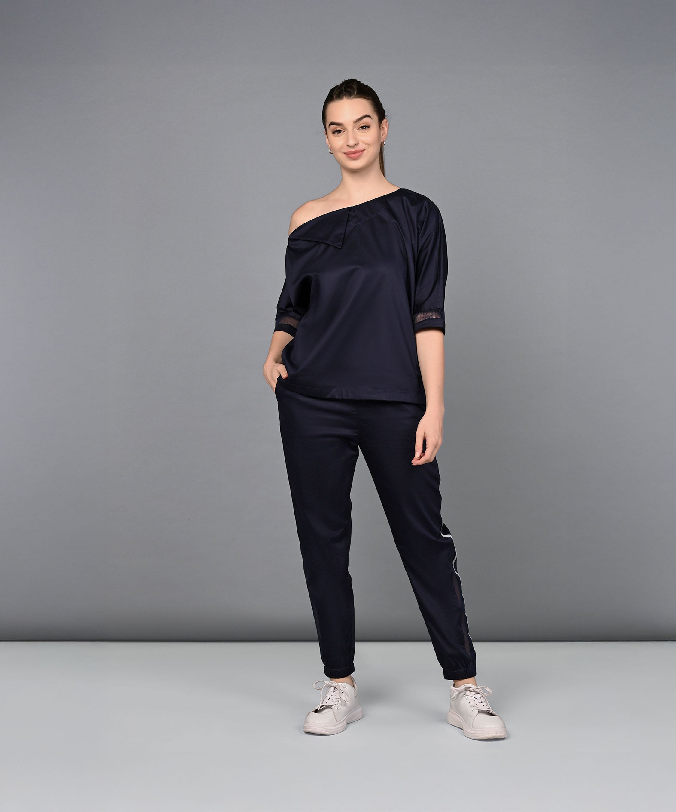 A woman wearing the Off Shoulder Nebula Navy Co-ord set, made from 100% cotton, stands and smiles against a plain gray background.