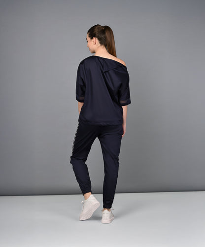 A woman wearing the Off Shoulder Nebula Navy Co-ord set, crafted from 100% cotton and paired with white sneakers, stands with her back to the camera against a gray background.
