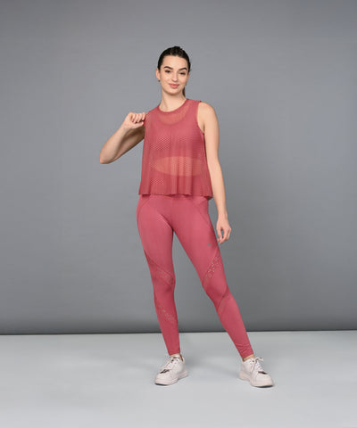 A woman models Peony Pink Leggings with a pink mesh tank top, posing gracefully against a plain gray background.