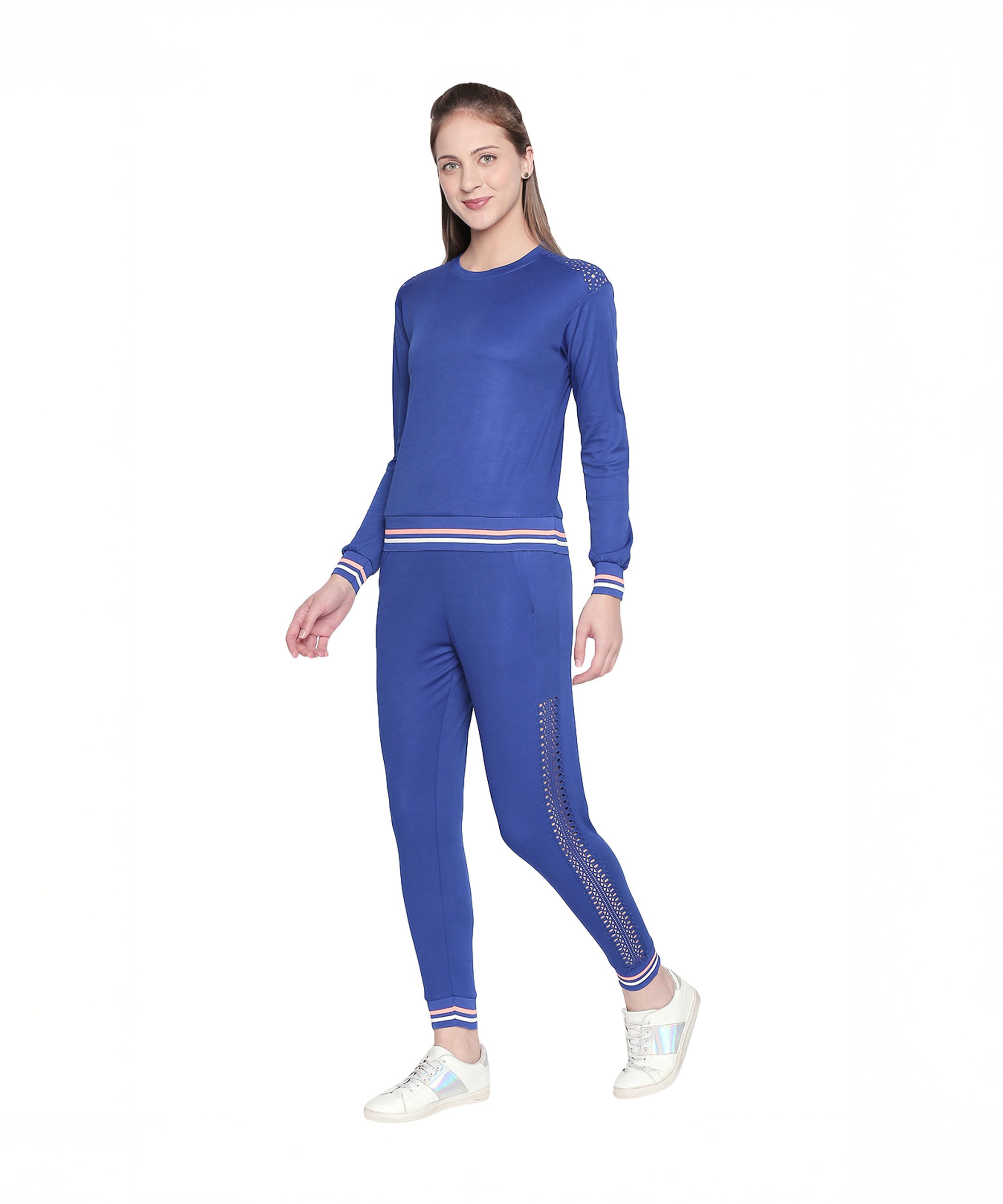A woman smiles on a white background wearing a Royal Blue Color Regular Fit Round Neck Full Sleeve Sweat Top with matching tracksuit, studded embellishments, and white sneakers for a sporty-chic look.