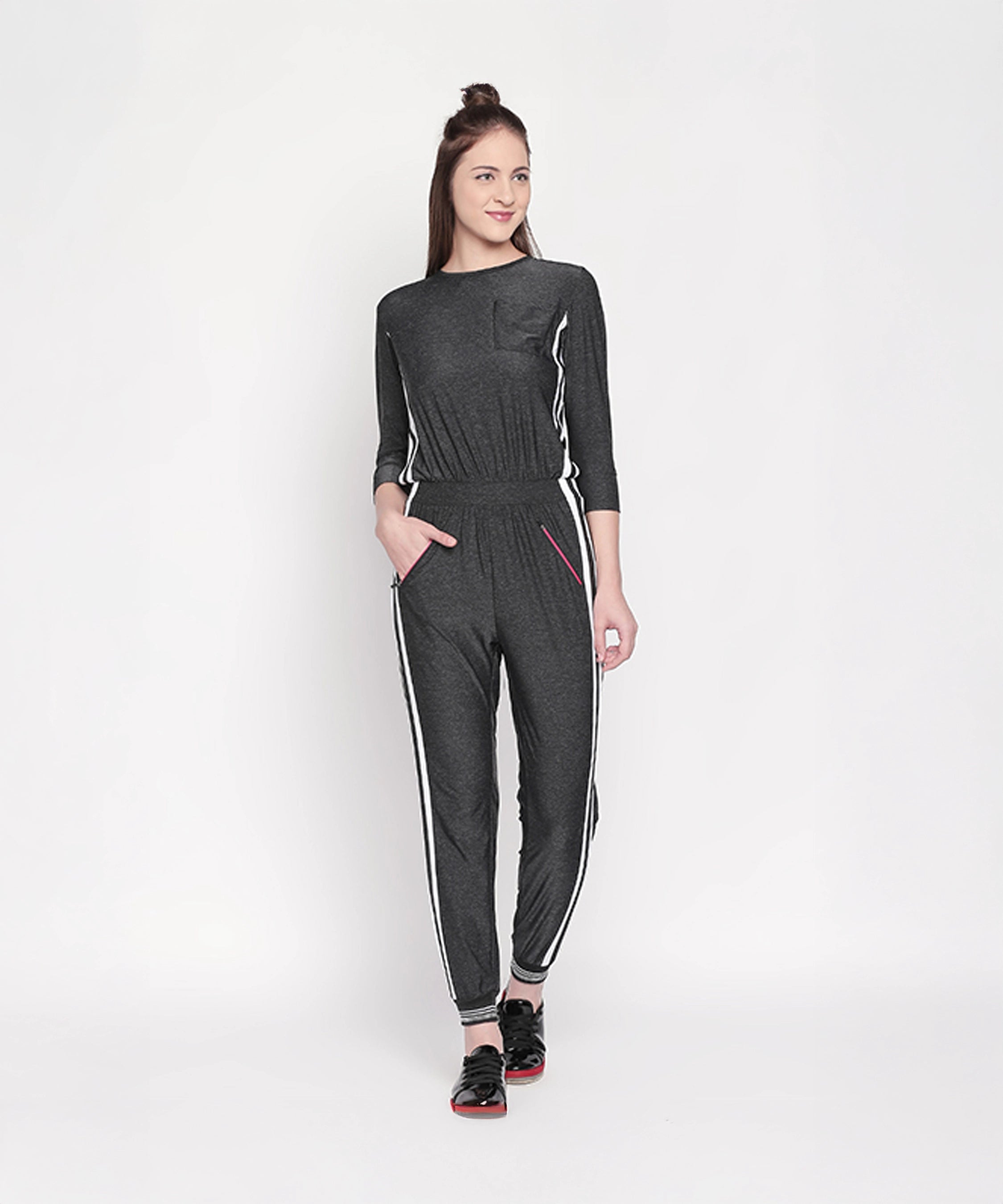 Woman wearing the Side Strips Grey Athleisure Jumpsuit with white stripes and zipper pockets, standing and smiling against a plain white background.