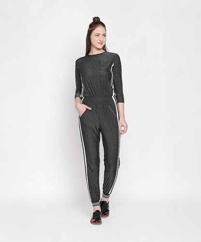 Woman wearing the Side Strips Grey Athleisure Jumpsuit with white stripes and zipper pockets, standing and smiling against a plain white background.