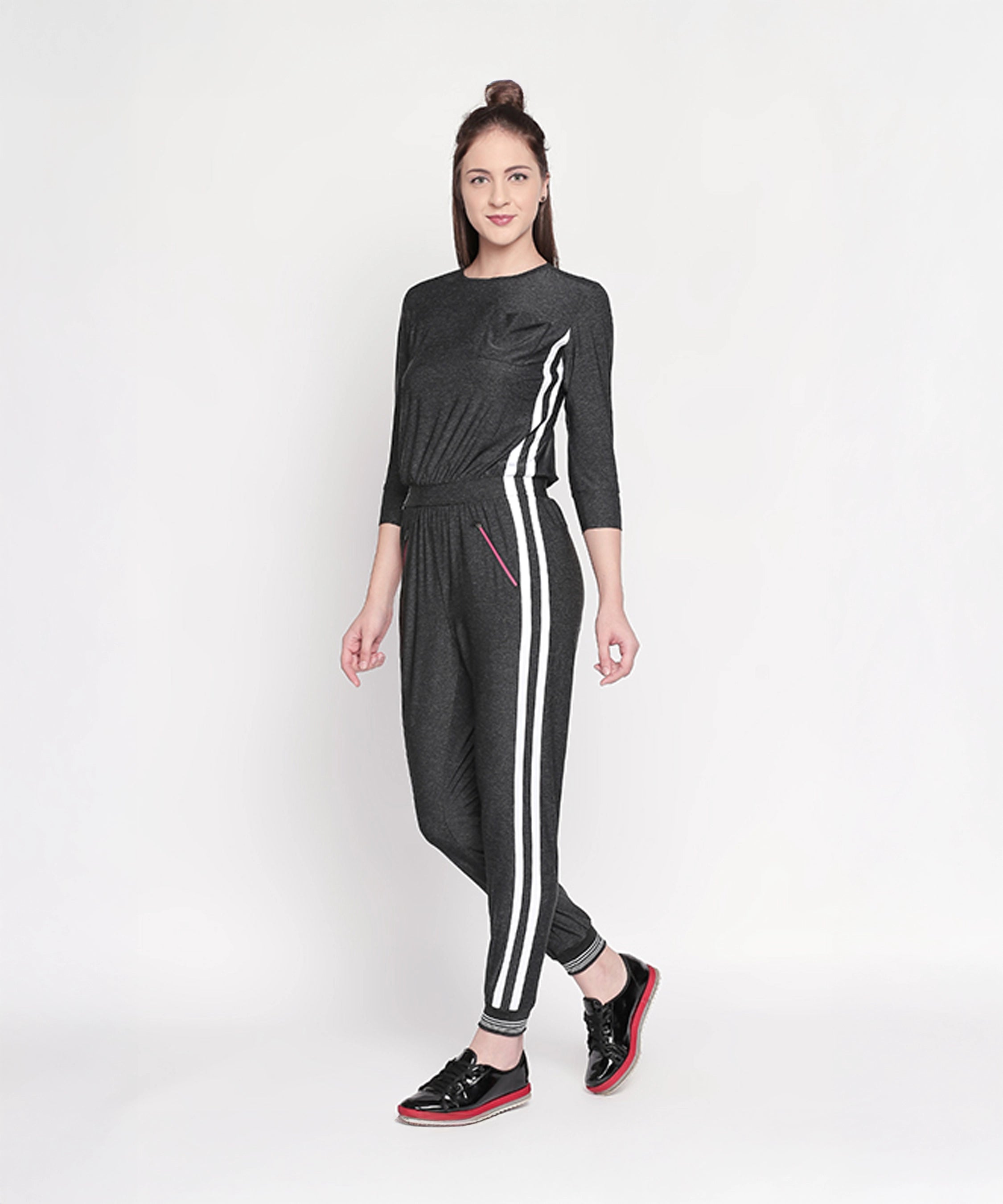 Woman wears the Side Strips Grey Athleisure Jumpsuit with white stripes and zipper pockets, posing against a plain white background.