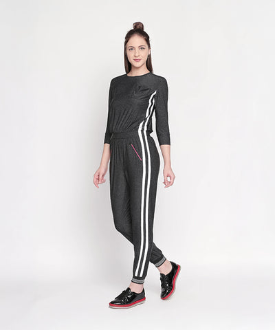 Woman wears the Side Strips Grey Athleisure Jumpsuit with white stripes and zipper pockets, posing against a plain white background.