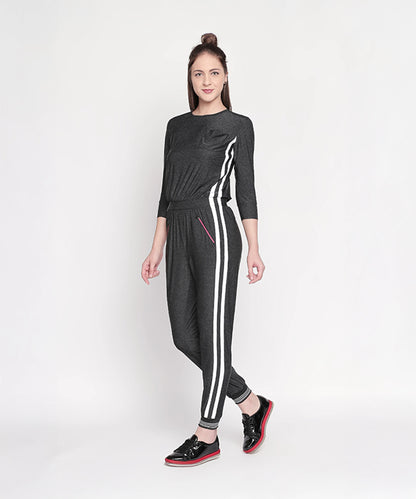 Woman wears the Side Strips Grey Athleisure Jumpsuit with white stripes and zipper pockets, posing against a plain white background.