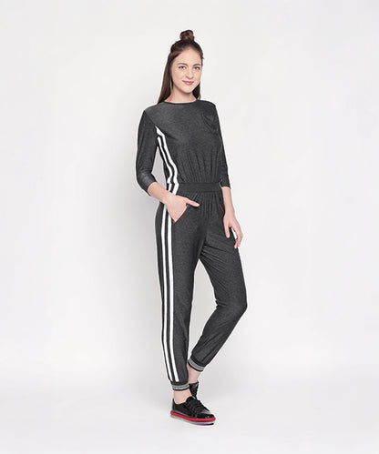 Woman in the Side Strips Grey Athleisure Jumpsuit, featuring white side stripes and soft fabric, poses with black sneakers against a plain white background.