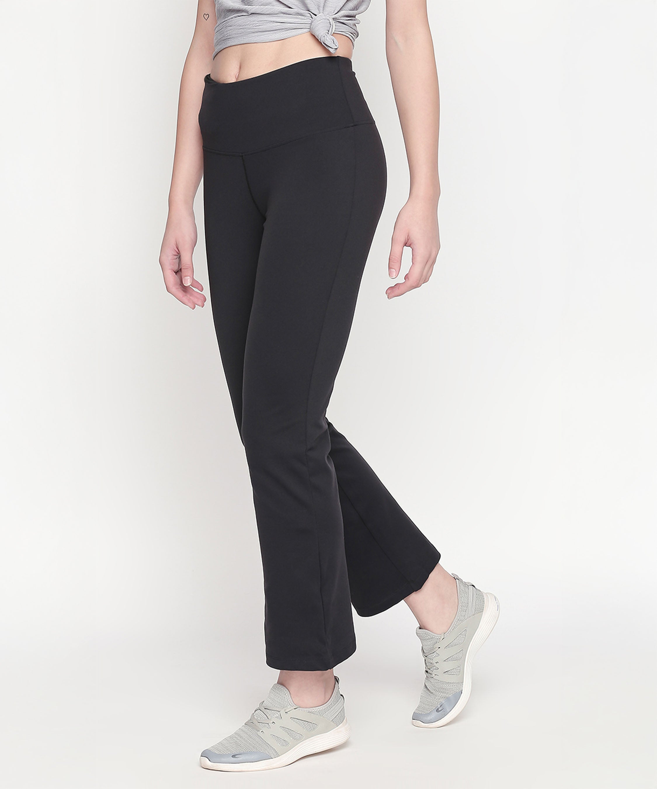 A woman stands against a white background wearing Bootcut High Waisted Workout Pants with a high-rise waistband, paired with a grey cropped top and grey sneakers.