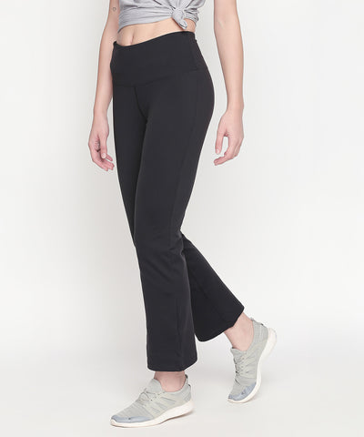 A woman stands against a white background wearing Bootcut High Waisted Workout Pants with a high-rise waistband, paired with a grey cropped top and grey sneakers.