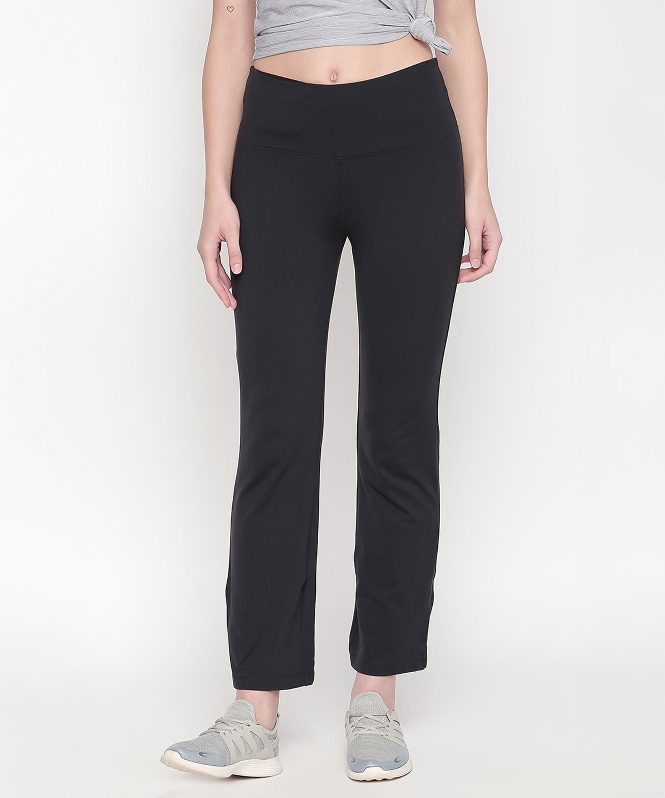 A woman stands against a white background wearing Bootcut High Waisted Workout Pants, paired with a grey crop top and grey sneakers.