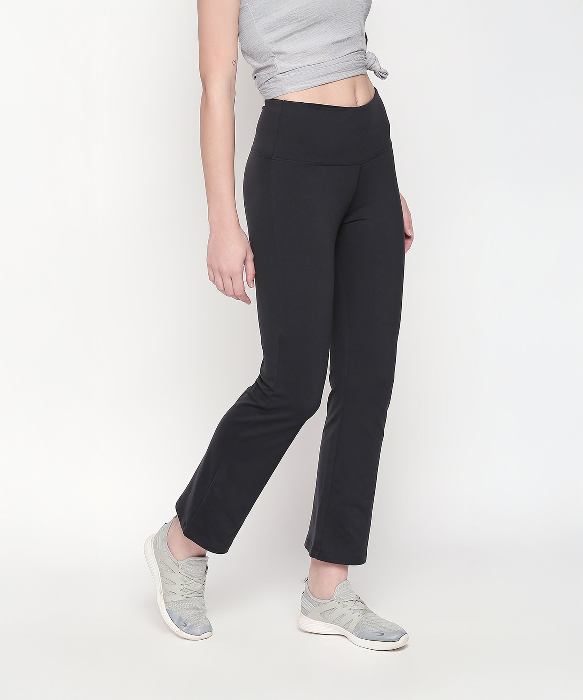 A person stands against a white background wearing Bootcut High Waisted Workout Pants with a high-rise waistband, paired with a gray top and gray sneakers.