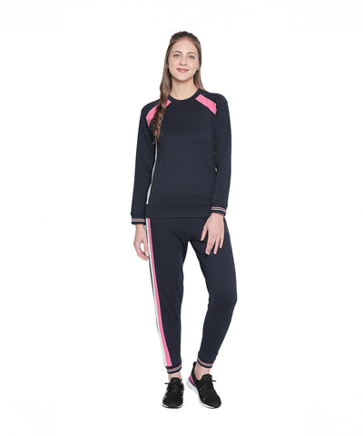 Woman standing and smiling against a white background, wearing navy blue joggers with a pink side stripe.