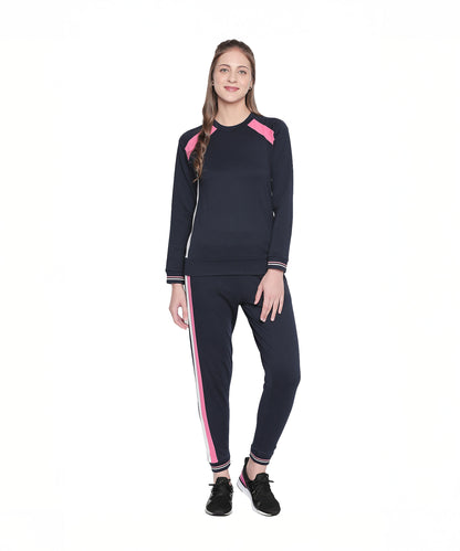 Woman standing and smiling against a white background, wearing navy blue joggers with a pink side stripe.