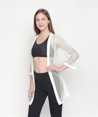 Woman models the Loose Fit 3/4th Sleeve White Shrug for Women over a black sports bra and leggings, posing and smiling to showcase an effortless athleisure style.