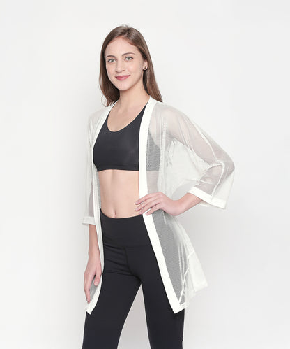 Woman models the Loose Fit 3/4th Sleeve White Shrug for Women over a black sports bra and leggings, posing and smiling to showcase an effortless athleisure style.