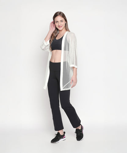 A woman models a Loose Fit 3/4th Sleeve White Shrug for Women over black sportswear against a plain white background for a chic, effortless athleisure look.