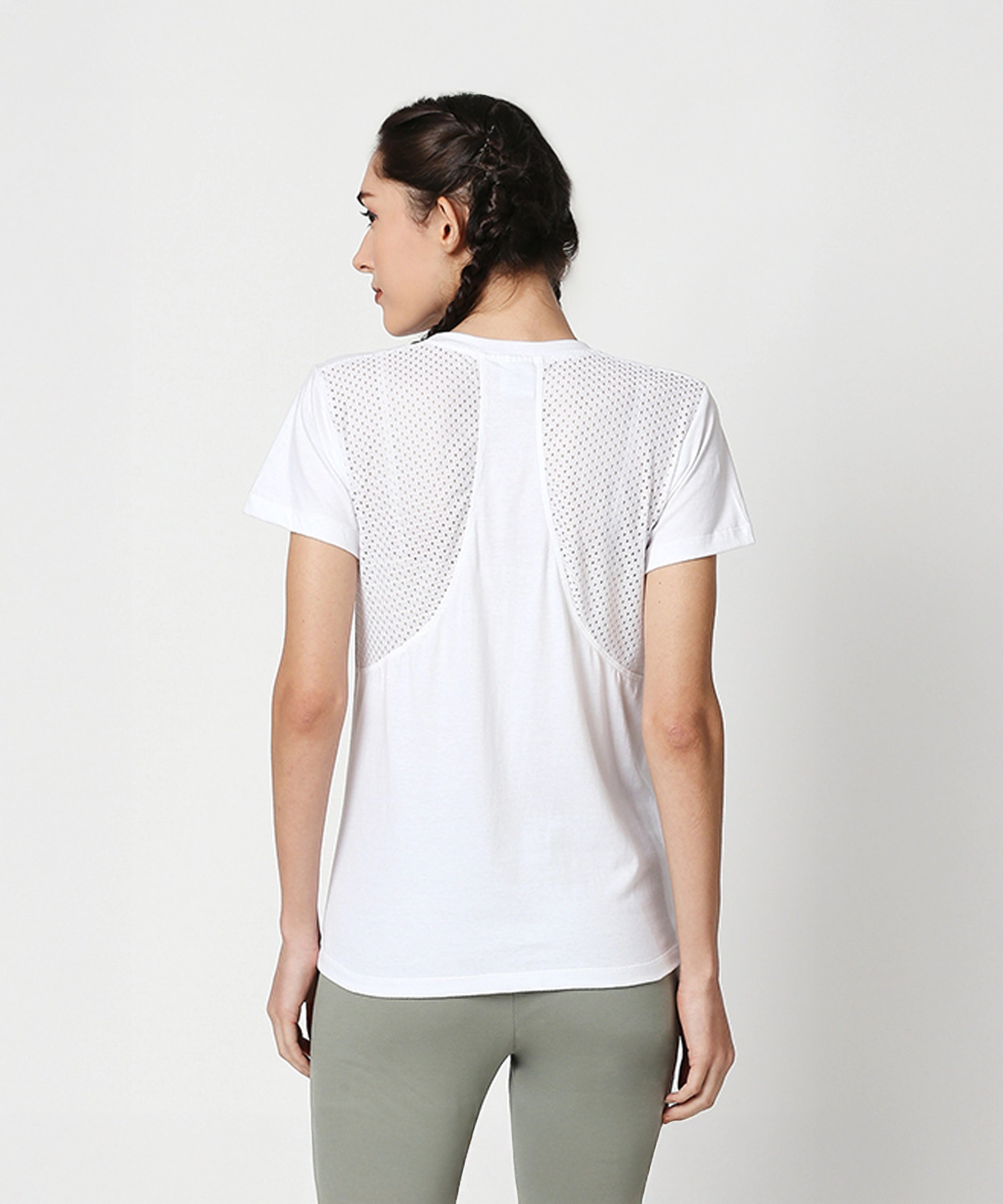 A woman faces away against a plain background, wearing a Duende Printed cotton tee with a mesh back and green leggings.