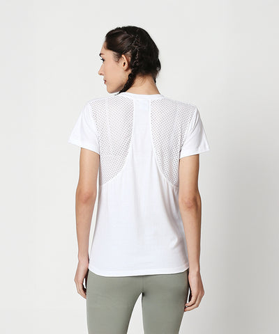 A woman faces away against a plain background, wearing a Duende Printed cotton tee with a mesh back and green leggings.