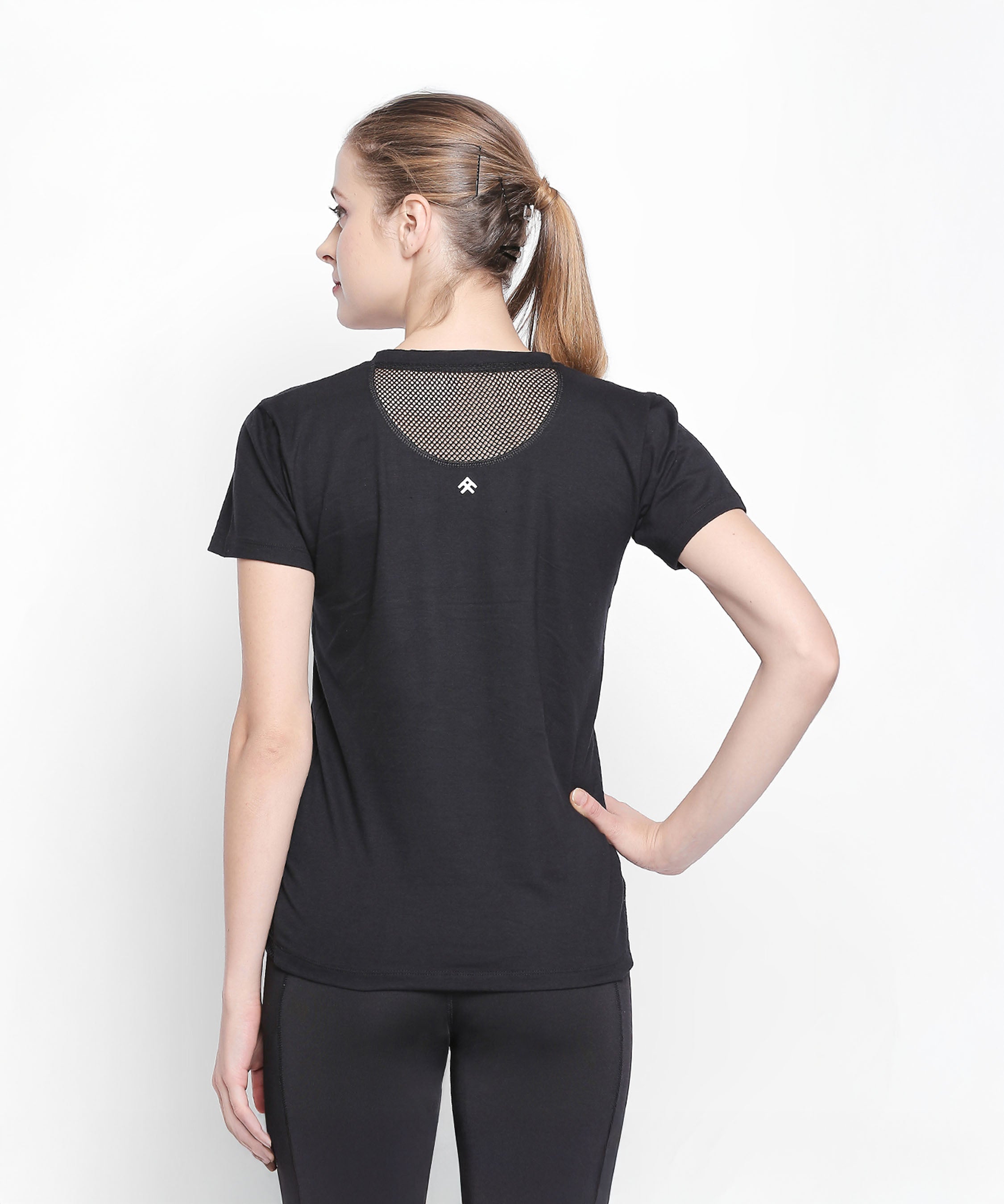 Woman with a ponytail, seen from behind with hand on hip, wearing the Tuna London Sara Basic Sports Tee With Net Detailing for Women against a white background.