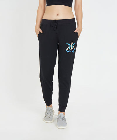 A person wearing Ashtanga Series Black joggers with a colorful logo, a black crop top, and gray sneakers.