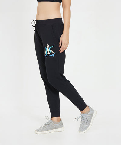 Woman wearing Ashtanga Series Black joggers featuring a blue and white flamingo print, paired with gray sneakers and a black crop top.