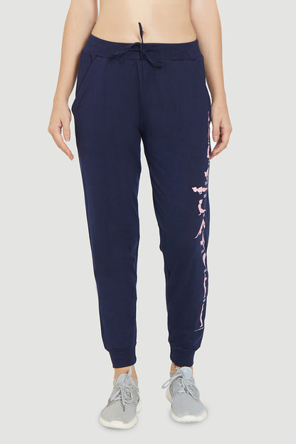 Stylish woman in Ashtanga Series Blue Joggers from TUNA LONDON with pink side print, paired with gray sneakers and a bare midriff, front view.