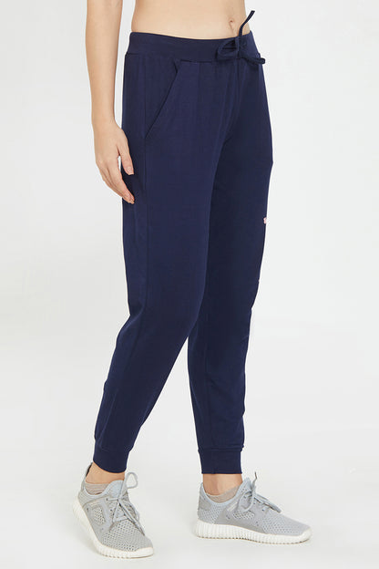 A fashionable woman wears Joggers - Ashtanga Series Blue by TUNA LONDON and light grey sneakers, standing against a plain white background.