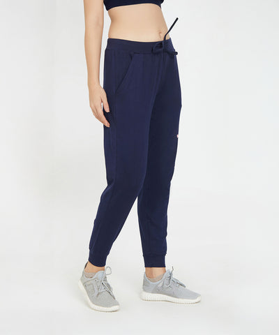 A person wearing Ashtanga Series Blue Joggers, gray sneakers, and a dark crop top stands against a white background.