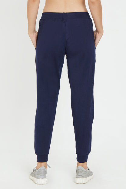 A stylish woman is seen from behind wearing Ashtanga Series Blue joggers by TUNA LONDON and gray sneakers, posed against a plain background.