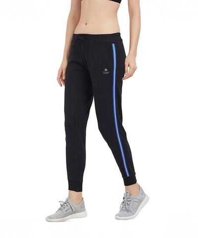 Woman wearing Classic Joggers TLC02SS, featuring a sporty side stripe and sleek tapered fit, paired with grey sneakers and a black sports bra, standing against a white background.