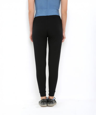 A person wearing Black Classic Joggers TLC02 with a slim tapered fit, a blue top, and patterned sneakers is standing facing away.