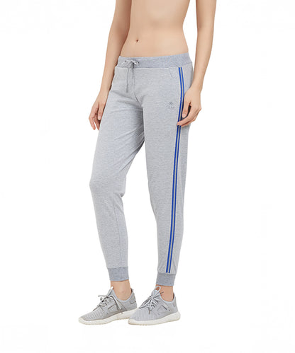 A person models the Side Stripe Joggers TLC03SS, featuring grey fabric with blue stripes, paired with grey sneakers against a white background.