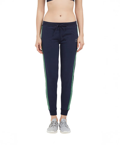 A woman stands front-facing in regular-fit navy Side Stripe Joggers TLC04SS with green side stripes, a sports bra, and gray sneakers. These comfy joggers are ideal for everyday wear.