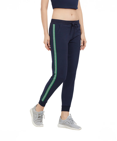 A woman models the Side Stripe Joggers TLC04SS in navy blue with green stripes, paired with gray sneakers and a navy crop top, set against a white background.