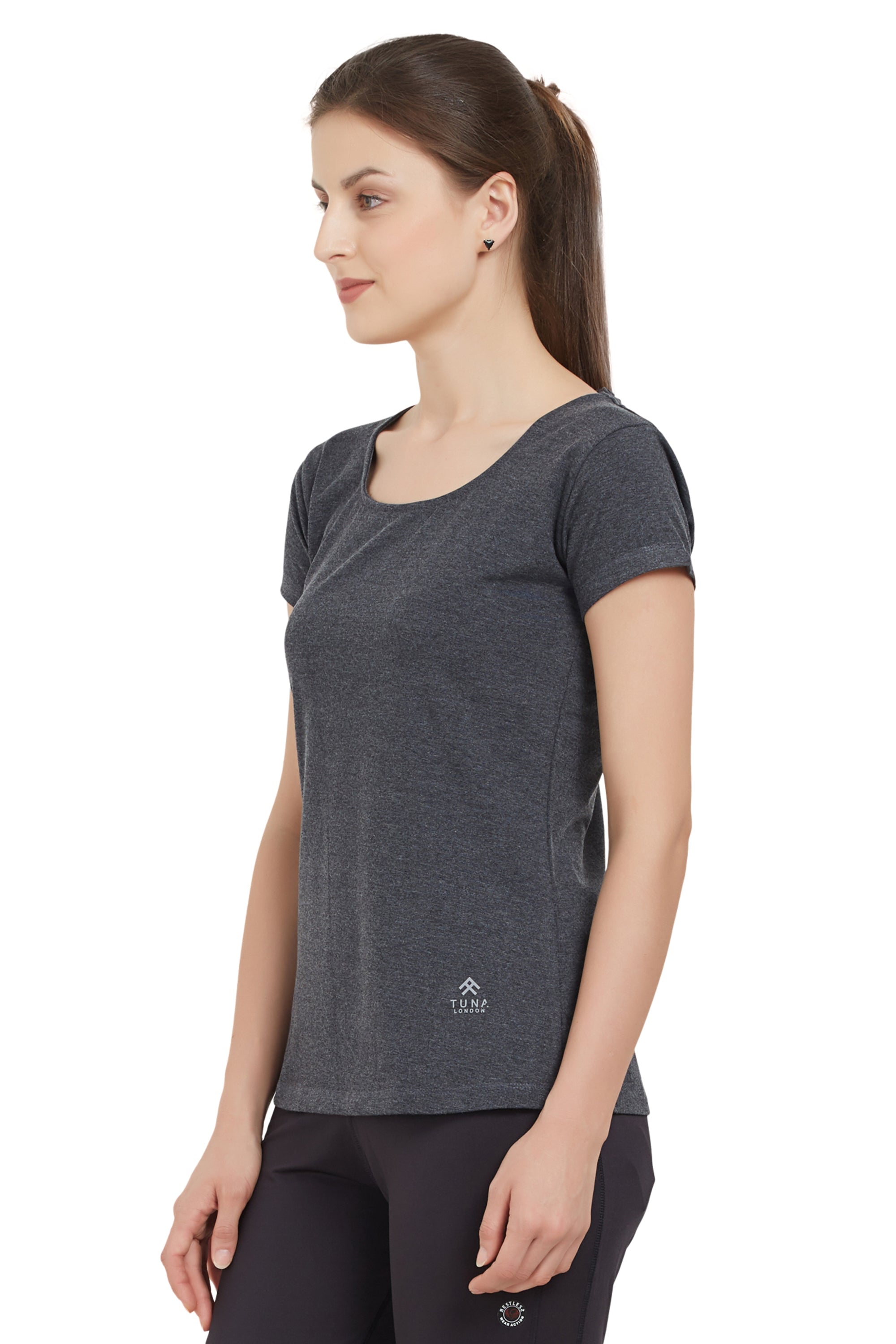 Woman in a Grey Round Neck Tee and black pants stands sideways, looking forward. The moisture-wicking fabric of the tee ensures comfort throughout the day.