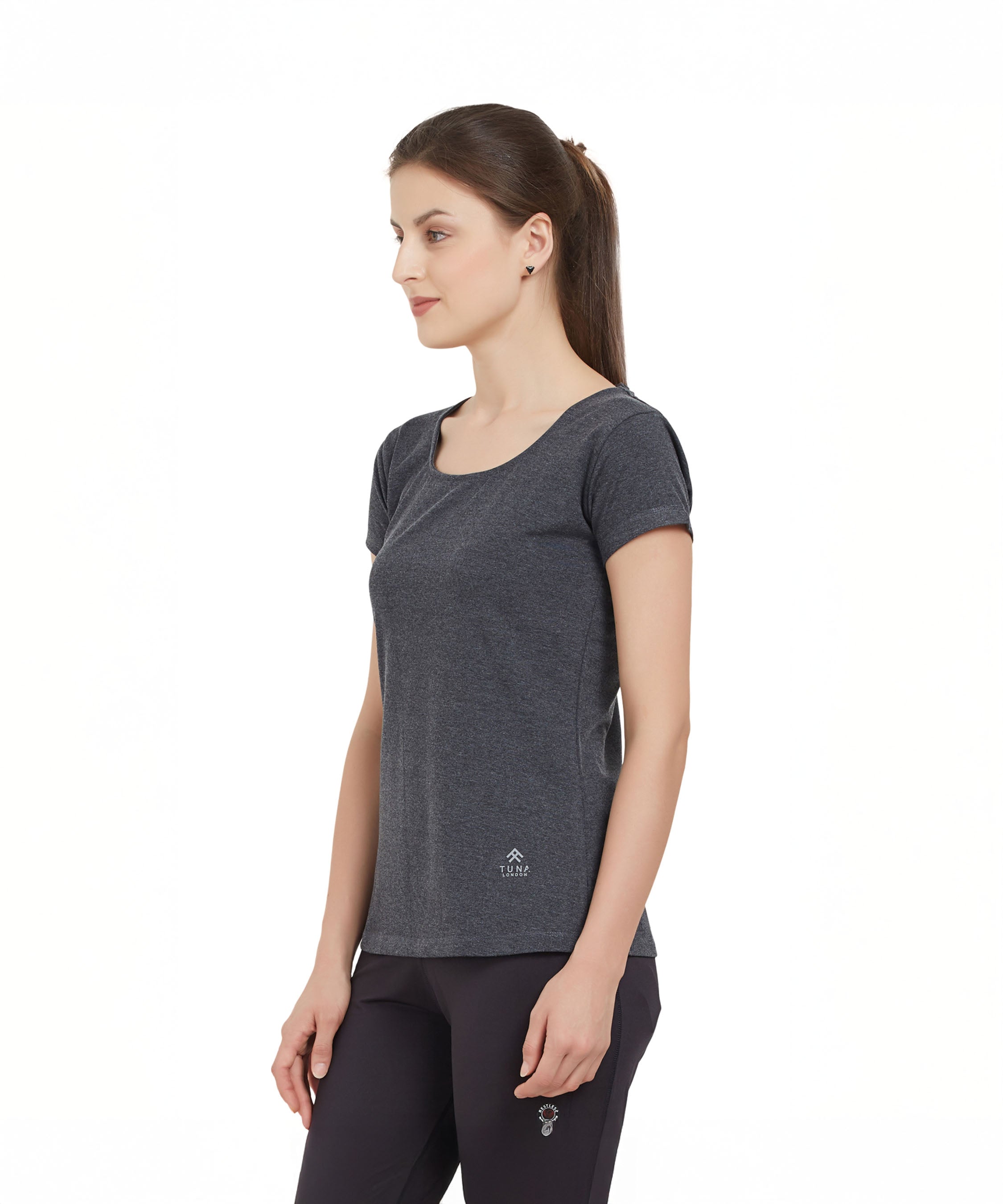 Woman in a Grey Round Neck Tee from TUNA LONDON stands sideways against a white background.