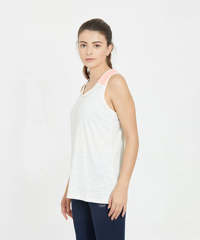 A woman wearing a White Sleeveless Tank Top and navy pants stands against a plain white background.