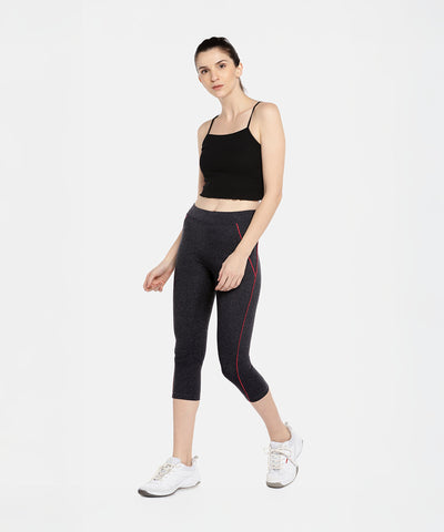 Woman in a black crop top, Classic Capri TLC67GRY yoga capris in gray with red accents, and white sneakers poses against a white background.