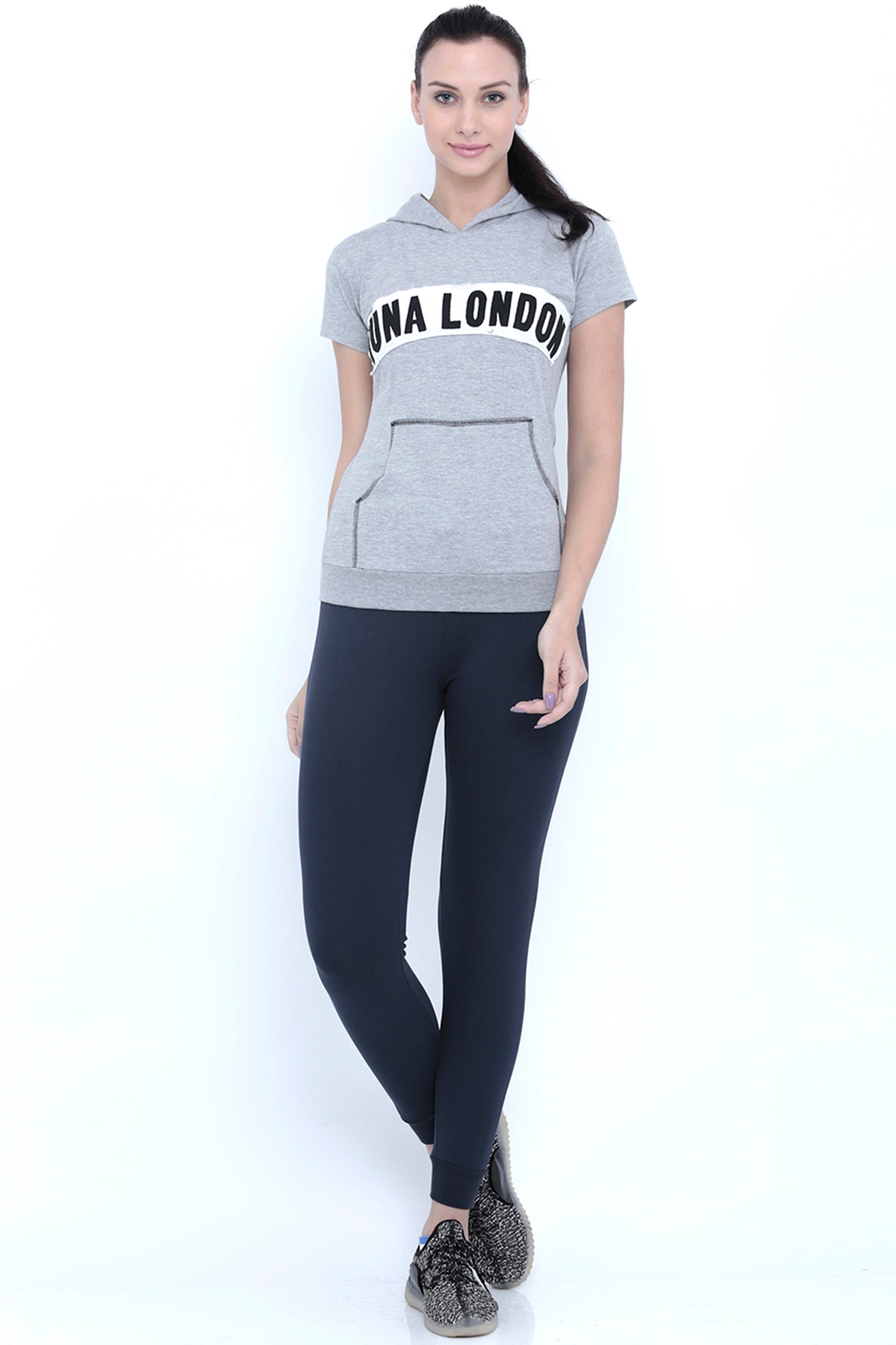 Fitness-conscious women will love this Grey Hoodie, made from 100% cotton and featuring "LUNA LONDON" text, perfectly paired with black leggings. She stands smiling confidently.