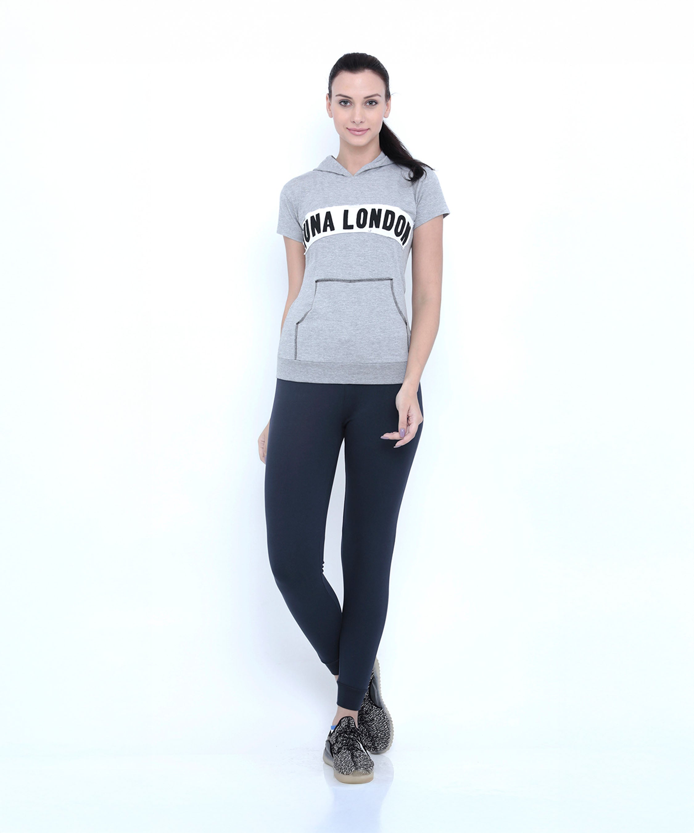 Fitness women will love this look: a woman in the Grey Hoodie with "LUNA LONDON" text, styled with black leggings and sneakers, stands against a white background.